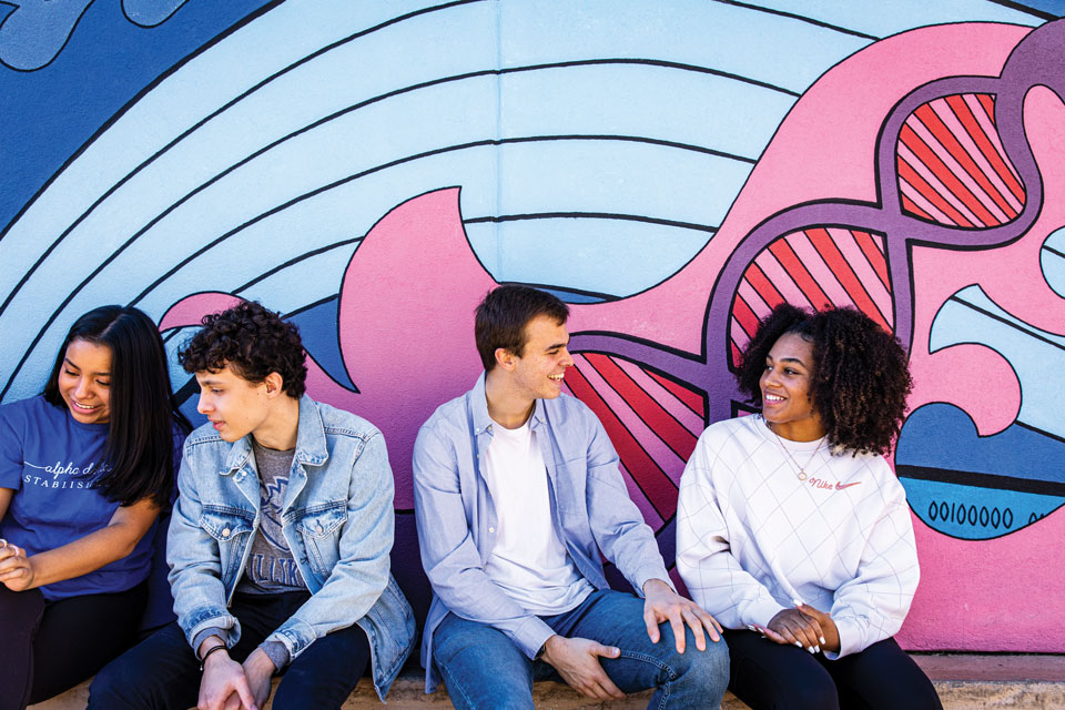 Four SLU students chatting in front of a painted mural