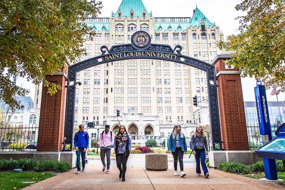 Students walk under an archway that says Saint Louis University on campus.