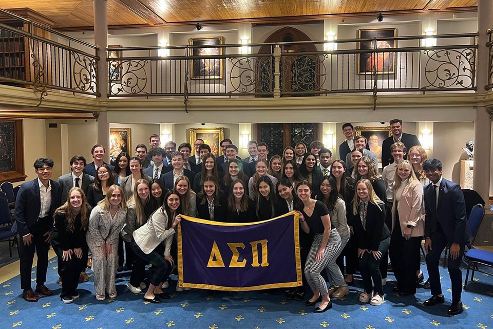 Members of the Delta Sigma Pi business fraternity pose for a class photo around their fraternity flag in the Marquette gallery