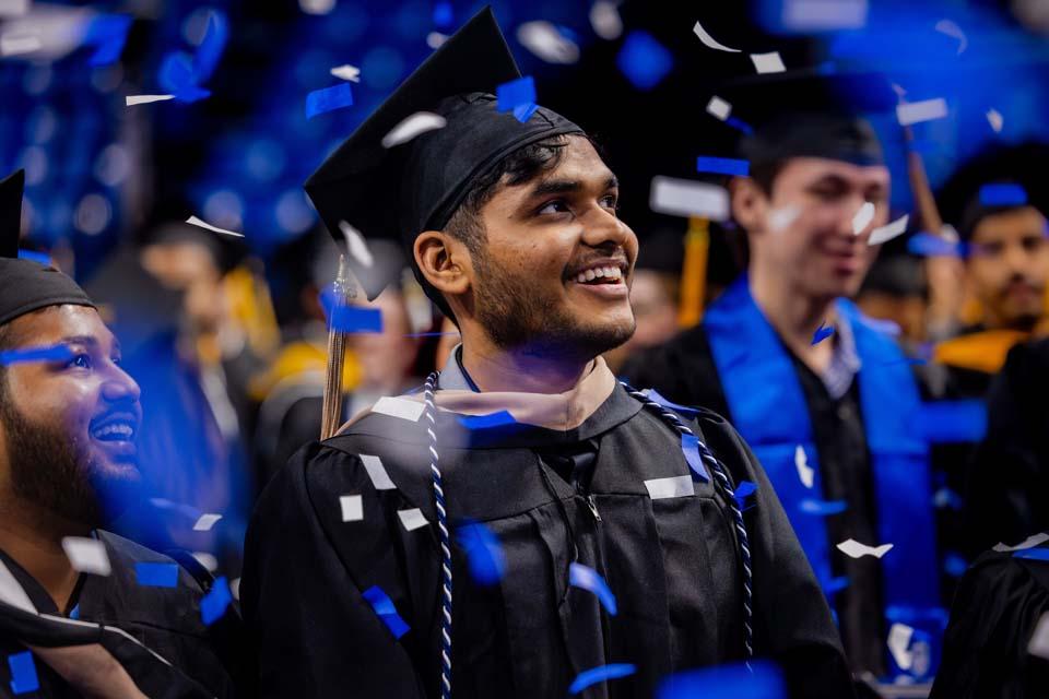 A graduate smiles as confetti falls around him during the 2025 Midyear Commencement ceremony