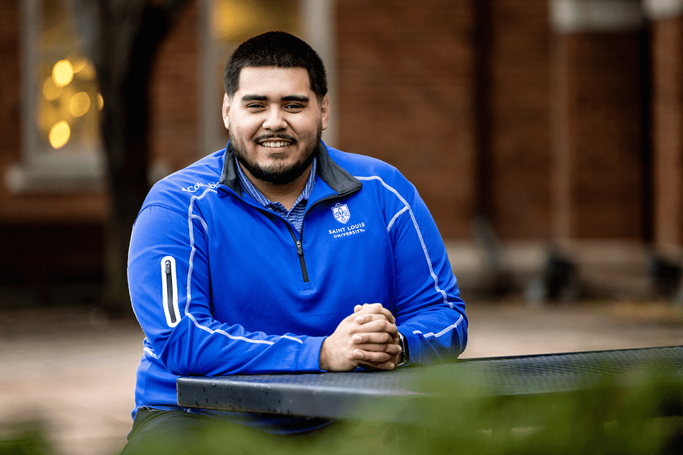 A student sits at a table outside of a brick building on campus.