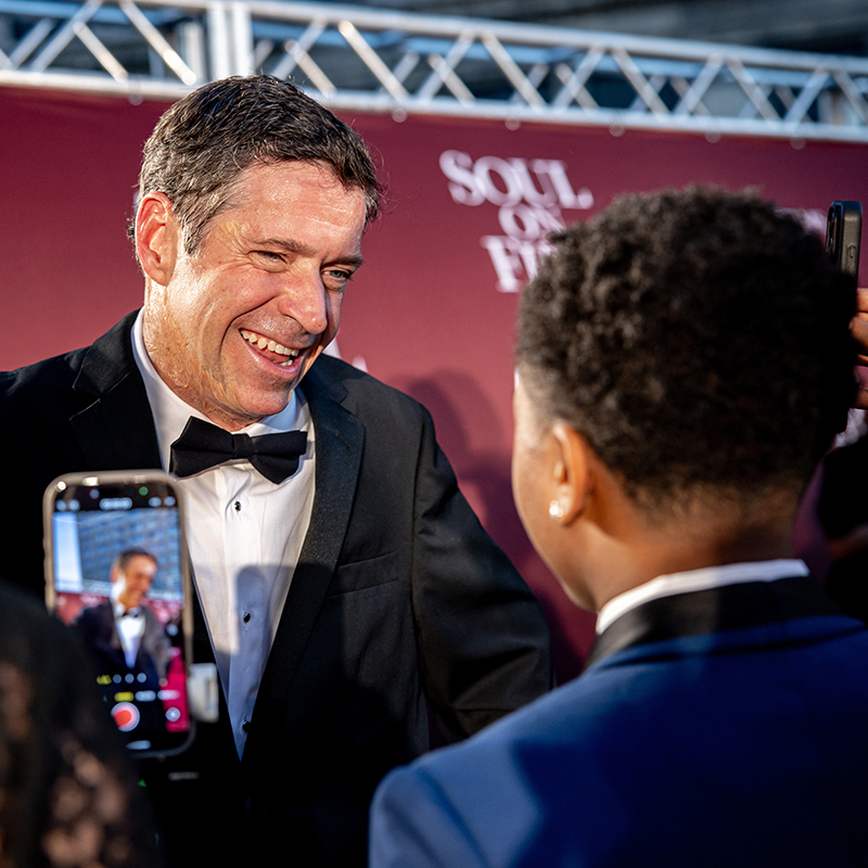 A man in a tux stands in front of a crowd. There's a banner in the back reading Soul on Fire.
