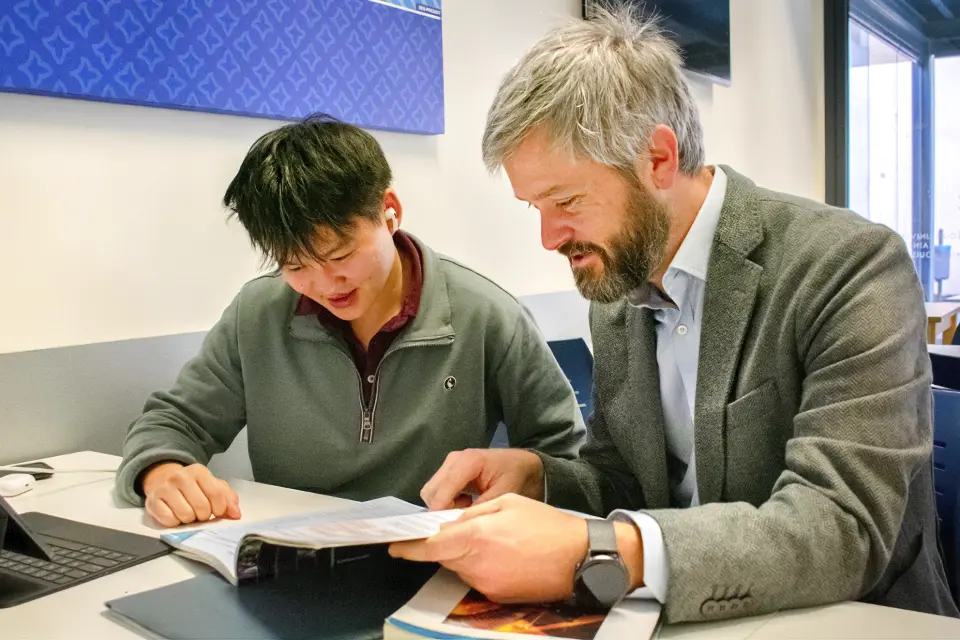 Student and professor sitting and looking at a book.