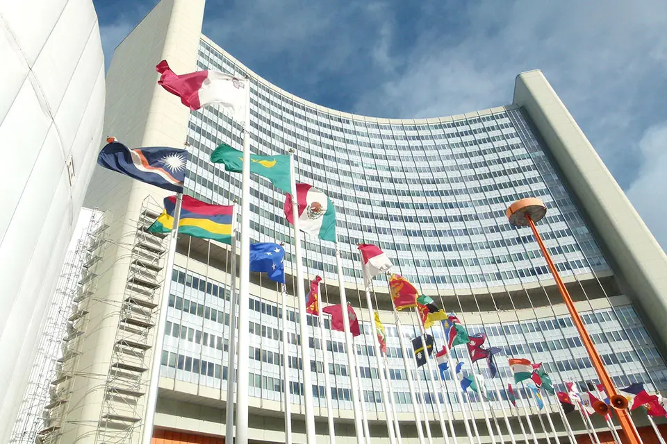 Rows of international flags fly in front of a tall office building.