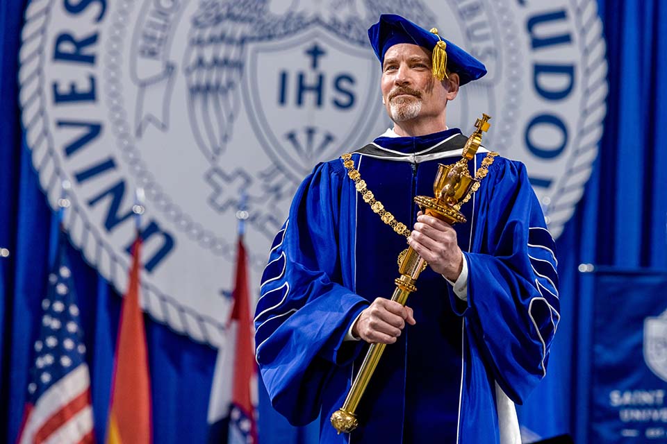 Feser Inauguration a man in a blue graduation gown holding a gold object