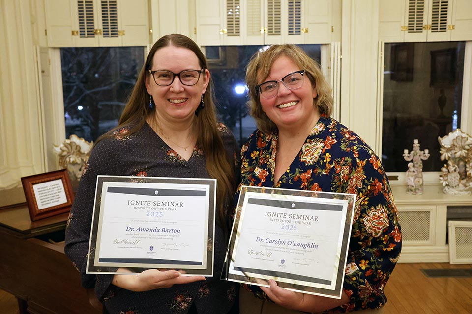 Two smiling women wearing glasses pose with their awards for a photo.