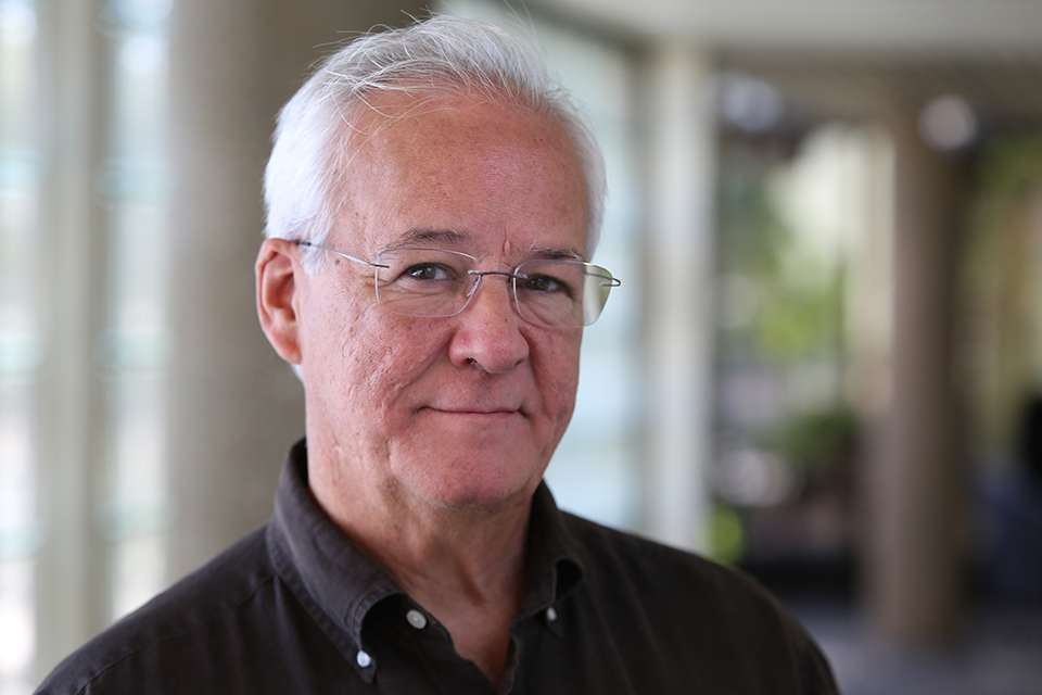 Professor Ricardo Wray stands in a hallway on Saint Louis University's campus smiling at the camera. 