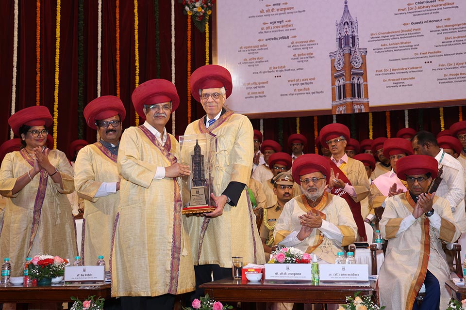 A diverse group of individuals in robes and red headgear at a ceremonial university event in India. 