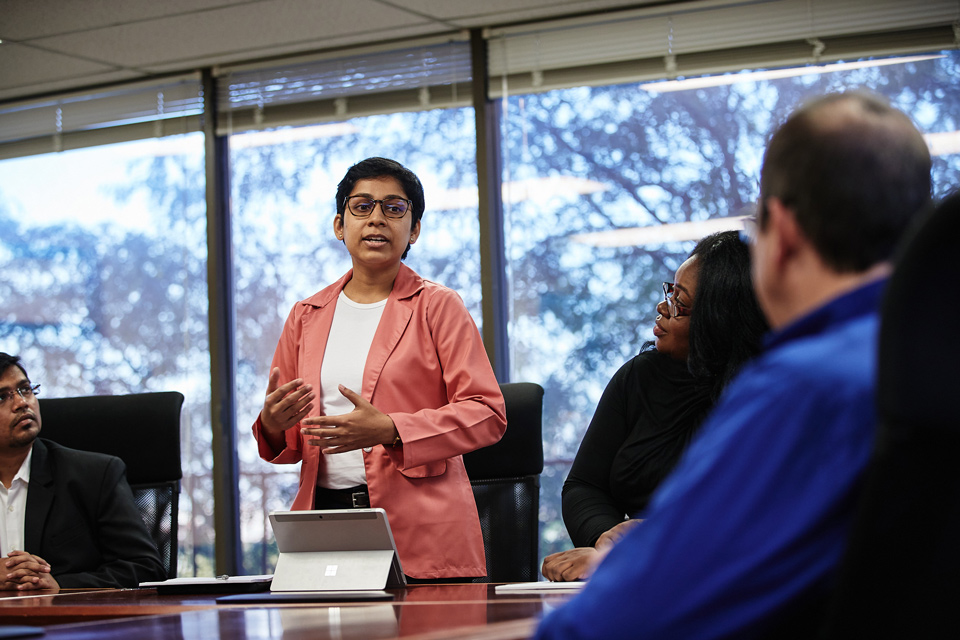 Students discuss their work with a professor in a conference room.